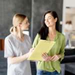 Lakeshore Bone & Joint Orthopedic Urgent Care | A healthcare professional in scrubs is holding a clipboard and talking to a woman in casual clothing inside a well-lit room.